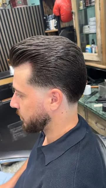 Cheveux coiffés en arrière et barbe courte taillée nette, vus de trois quarts