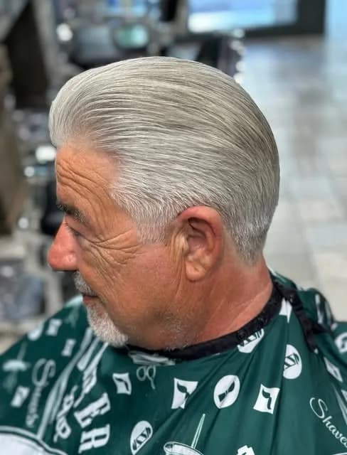 Coupe classique coiffée en arrière sur cheveux gris, client en cape noire et verte