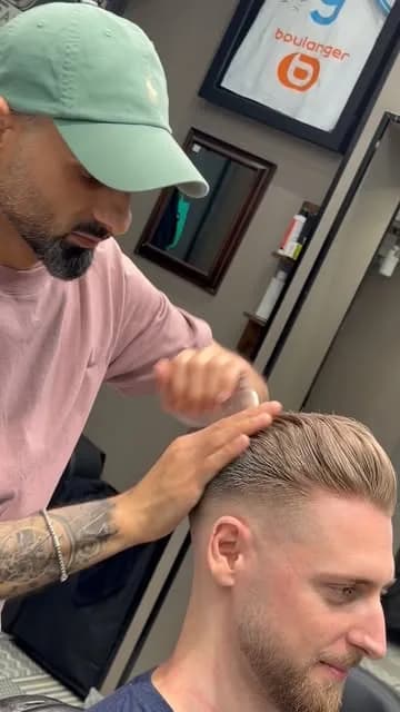 Le barbier, casquette verte, finit à la main le coiffage d’un dégradé
