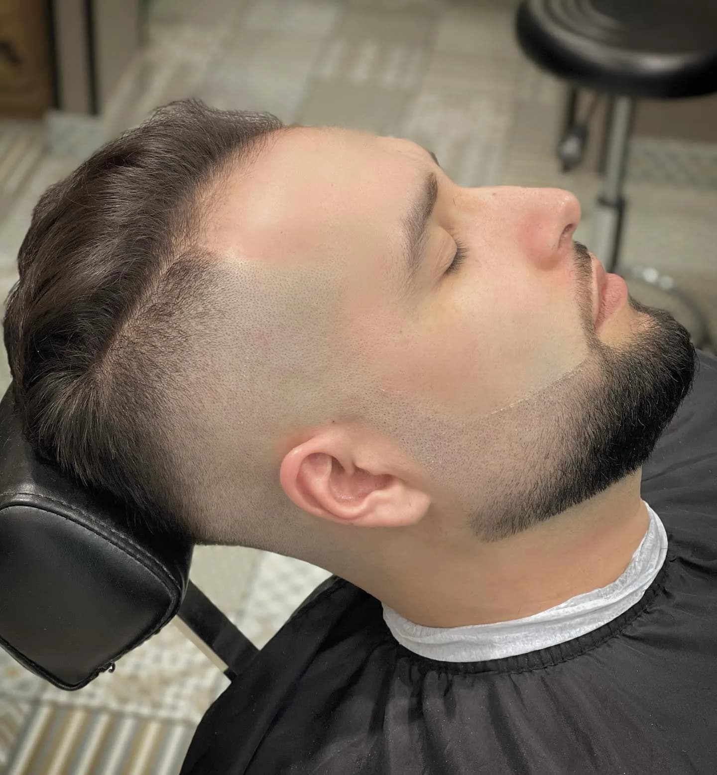 Client renversé dans le fauteuil, dégradé et barbe taillés de près, vu de profil