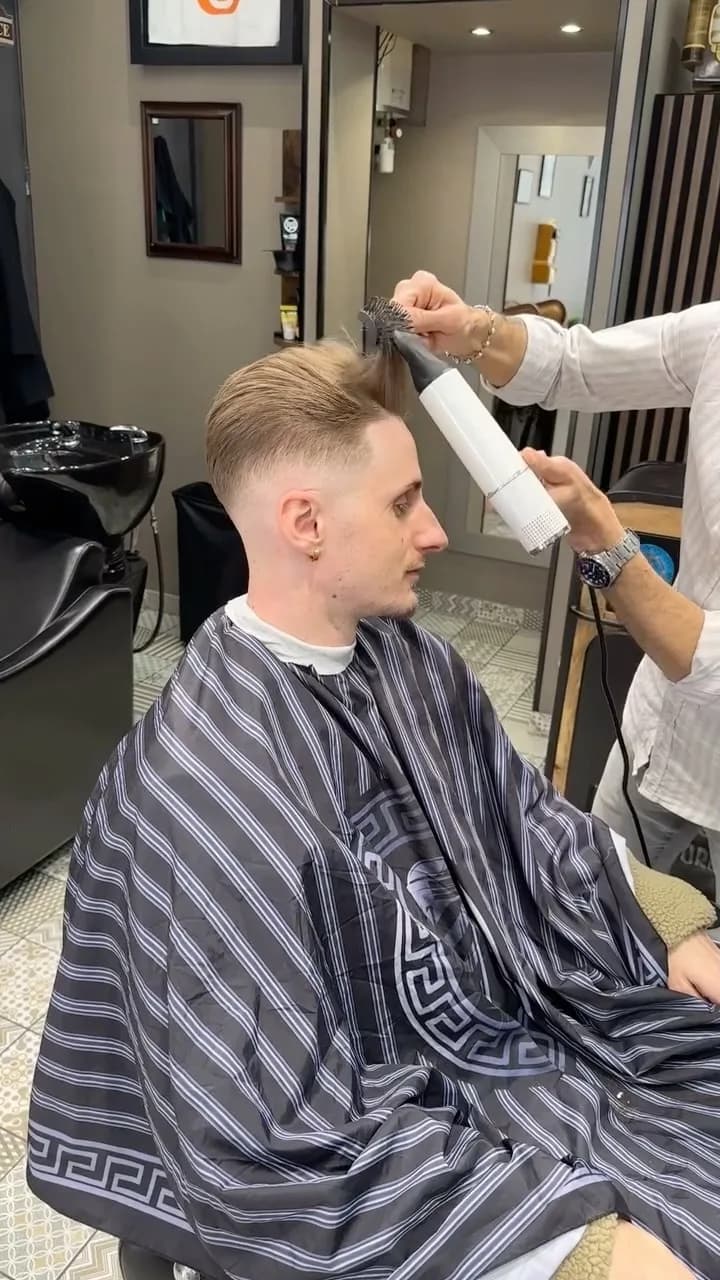 Finition au spray et à la brosse sur la coupe dégradée d’un client en cape rayée